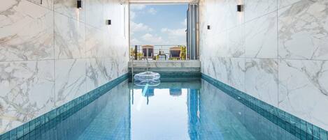 A swimming pool with a clear view of the sky through a large window, surrounded by marble walls.