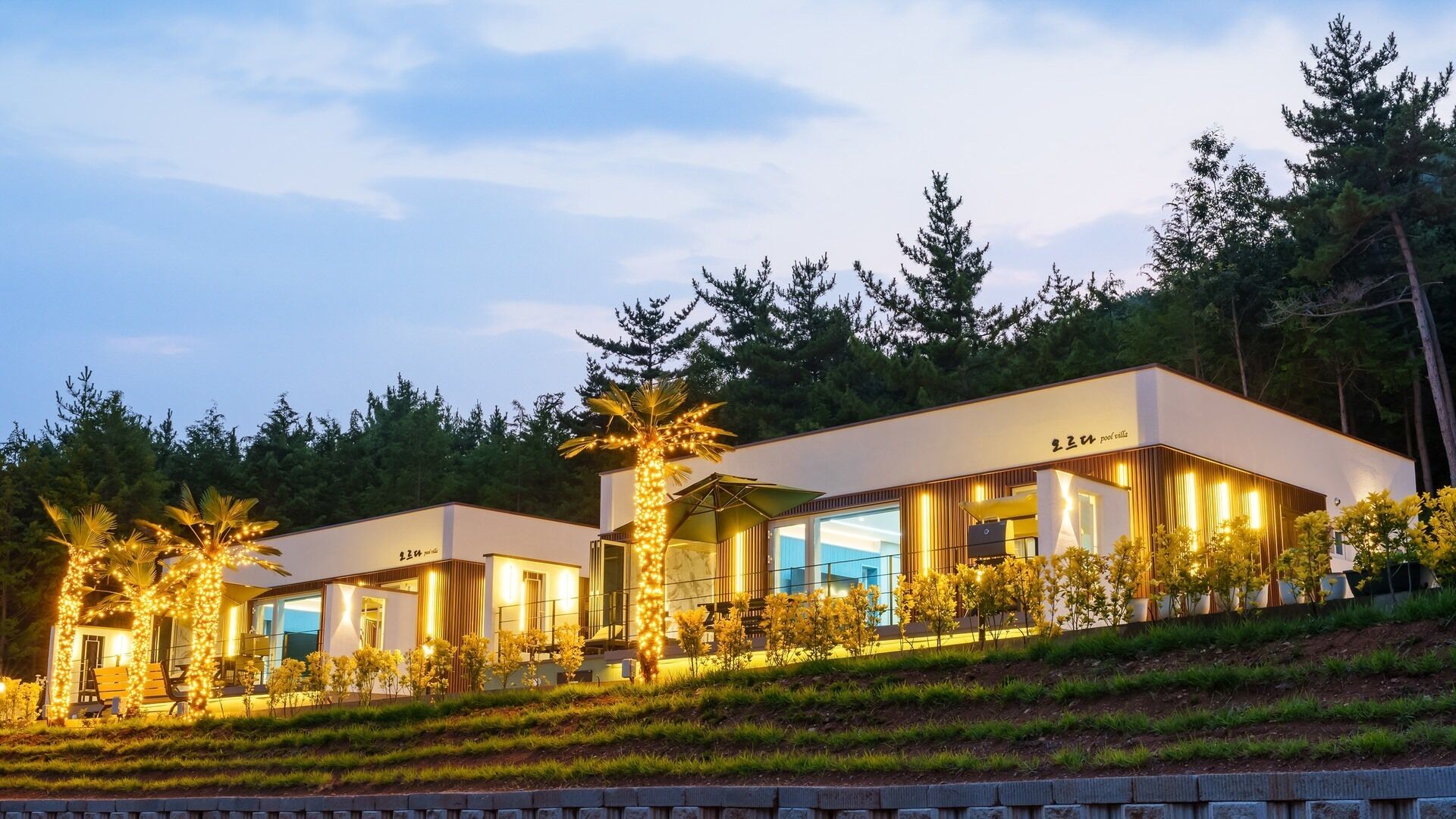 A modern hotel with a pool area, surrounded by trees and a landscaped garden.
