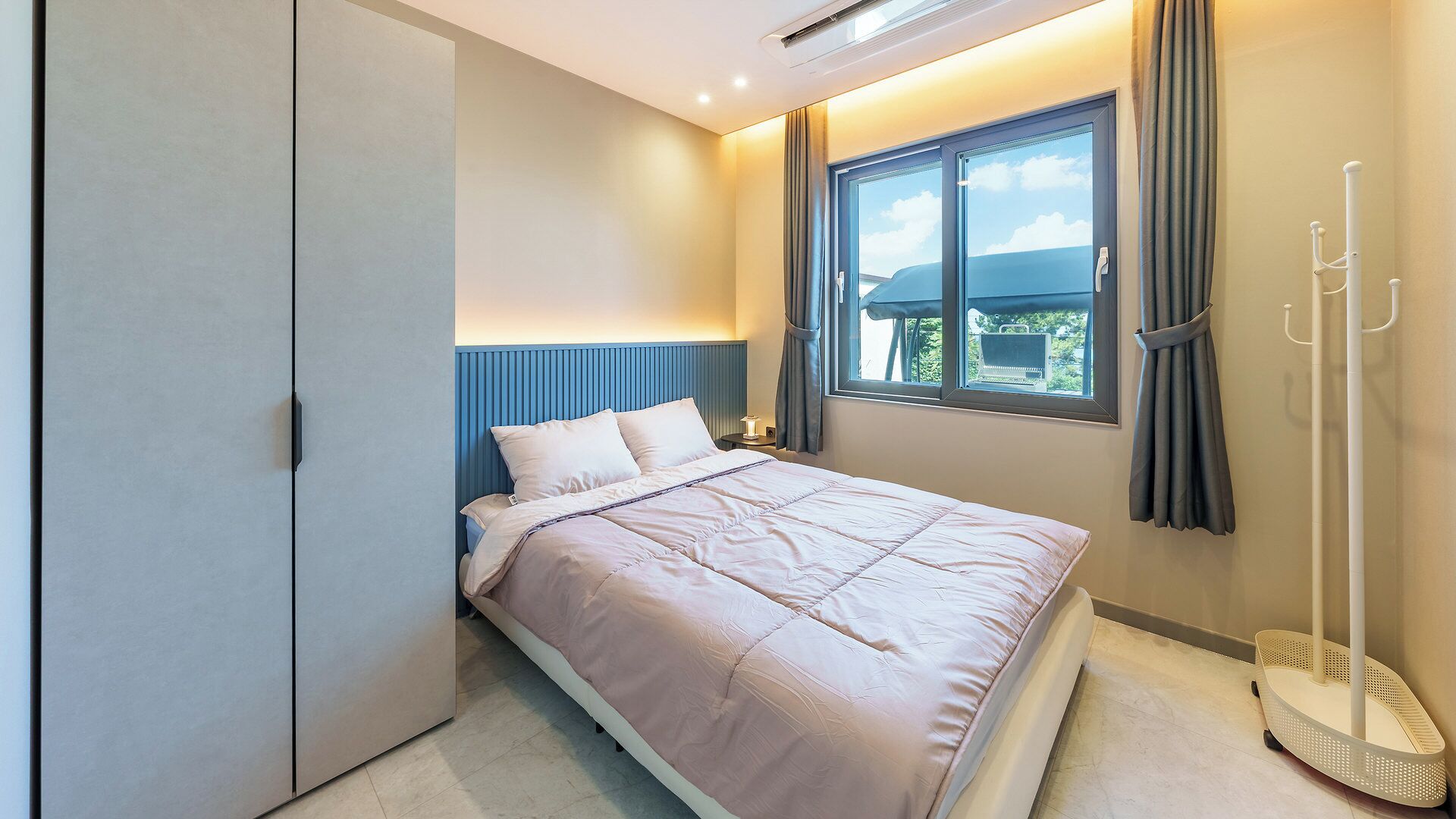 Una camera da letto ordinata con un letto, un comodino, una finestra con tende e una lampada da terra.