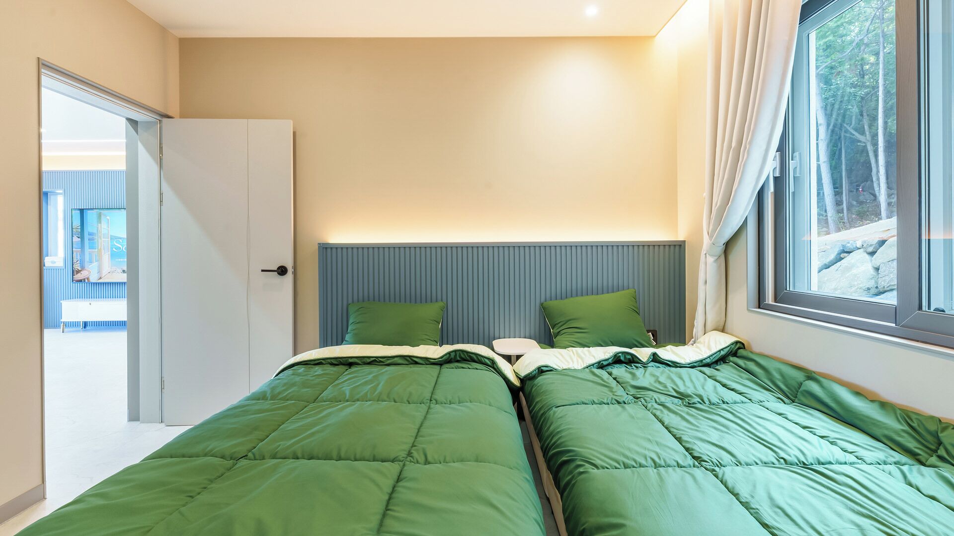 A bedroom with two beds, a window with curtains, and a door leading to another room.