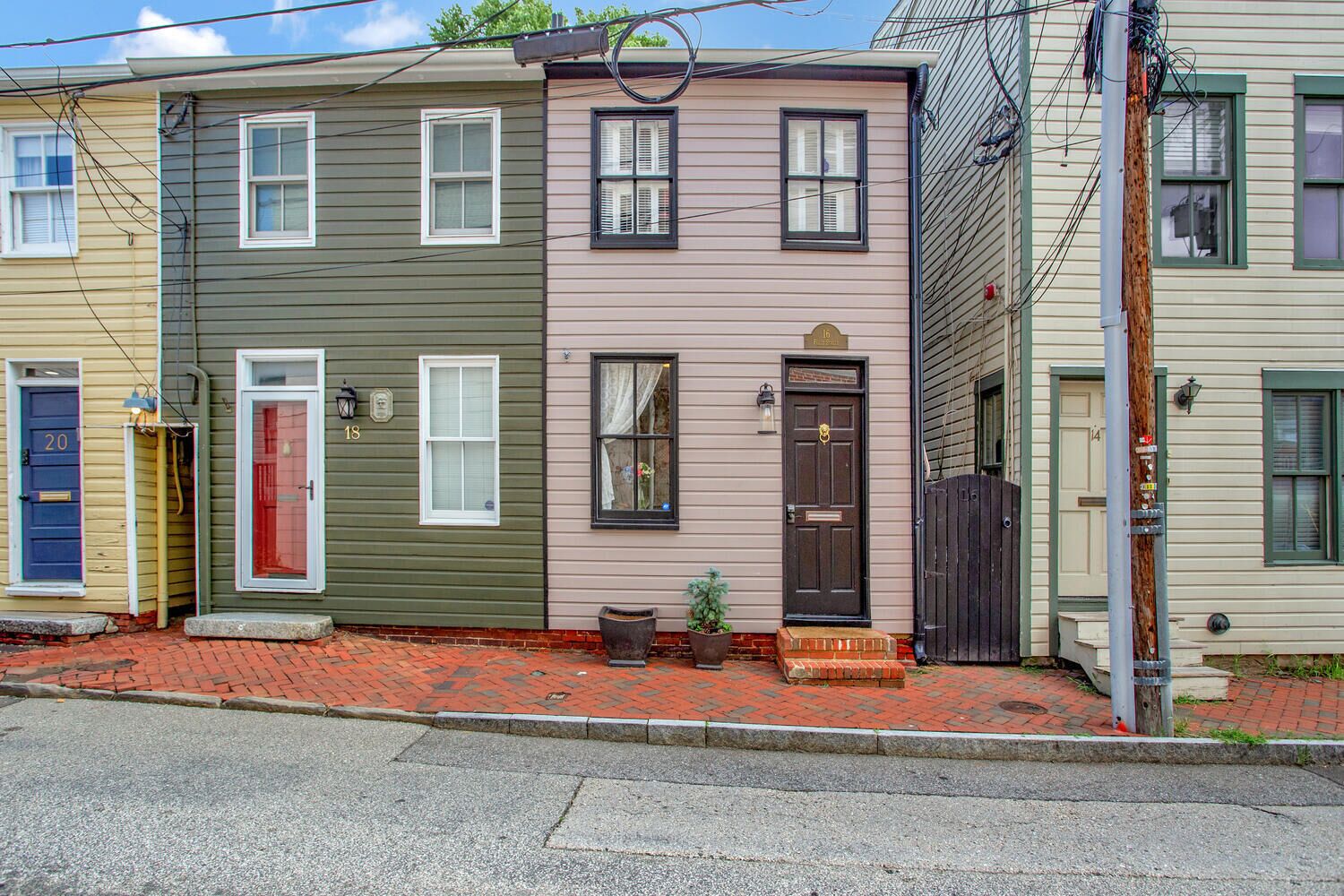A row of three-story townhouses with distinct front doors and windows, a brick sidewalk, and a utility pole with wires.
