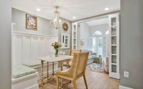 A dining area with a table, chairs, a bench, a chandelier, and a view into another room.