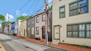 A row of colorful townhouses with a brick sidewalk and a street. - Historic Row Home in Downtown Annapolis (Annapolis)