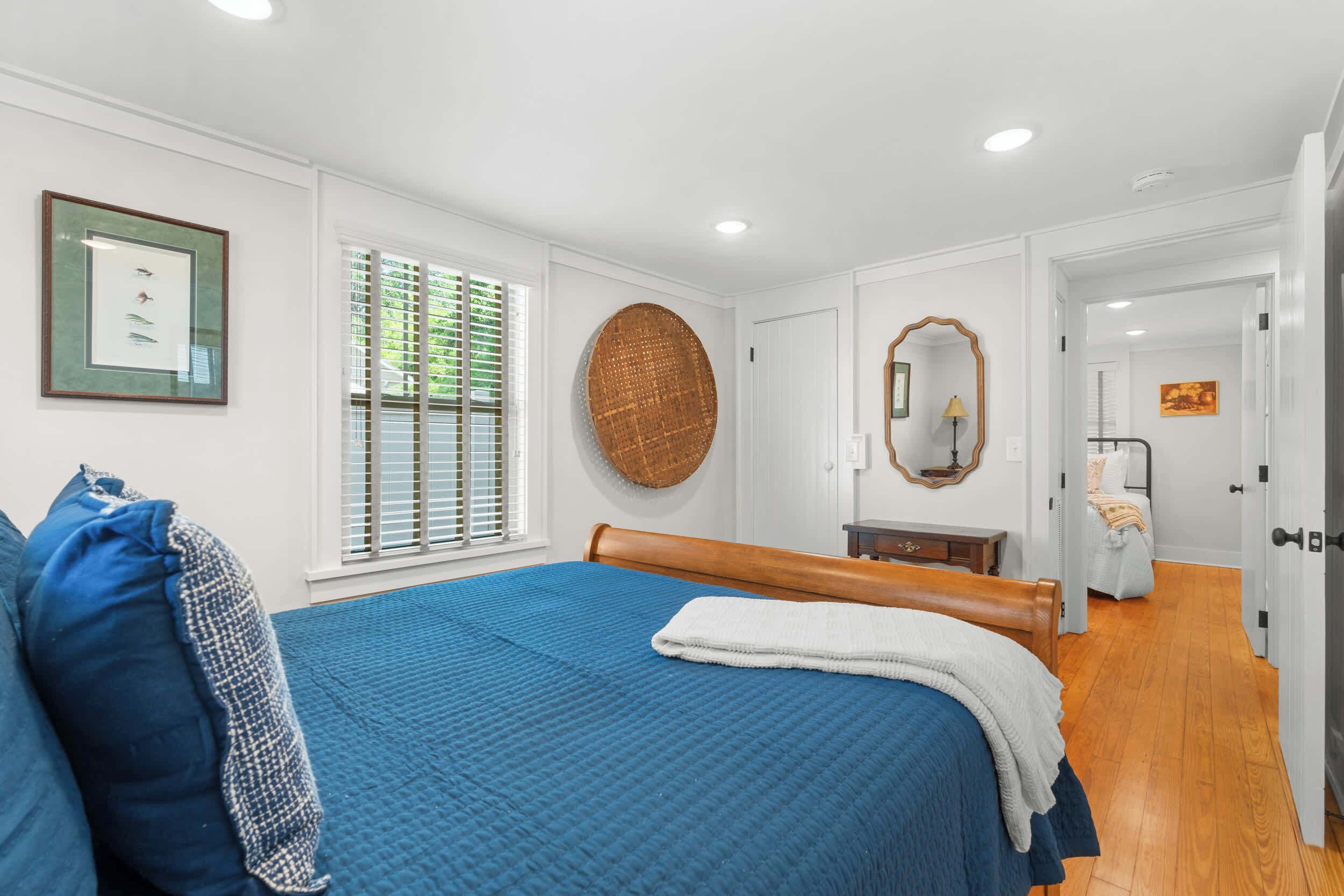 A bedroom with a large bed, a round woven wall hanging, a framed picture, and a mirror.