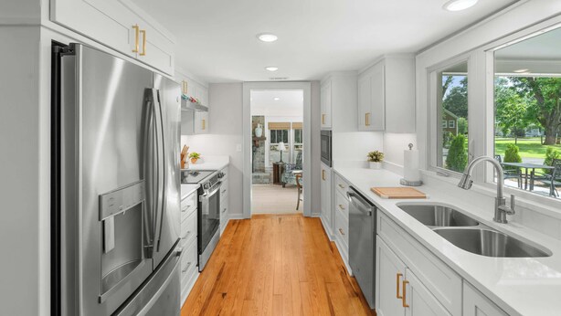 Una cocina moderna con electrodomésticos de acero inoxidable, armarios blancos y piso de madera.