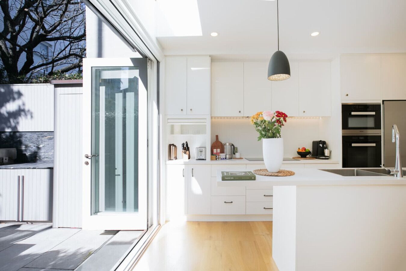 A modern kitchen with white cabinetry, a large island, a hanging pendant light, and a view of the outdoors.