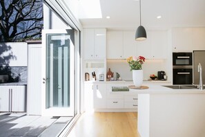 A modern kitchen with white cabinetry, a large island, a hanging pendant light, and a view of the outdoors.