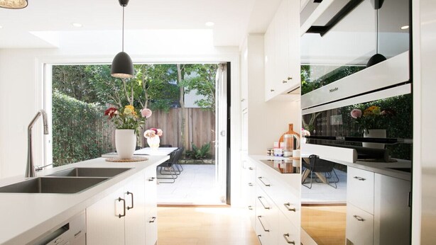Een moderne keuken met witte kasten, een centraal keukenblok en een eethoek met een tafel en stoelen.