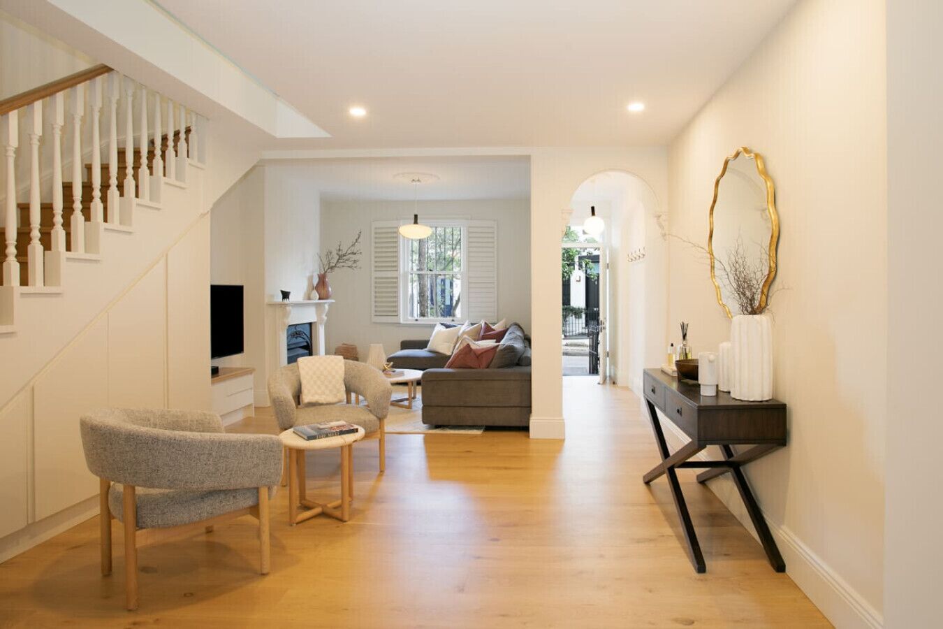 A spacious living area with a staircase, a sofa set, a coffee table, and a console table with decorative items.