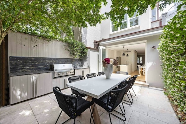 Un patio al aire libre con mesa, sillas y una parrilla.