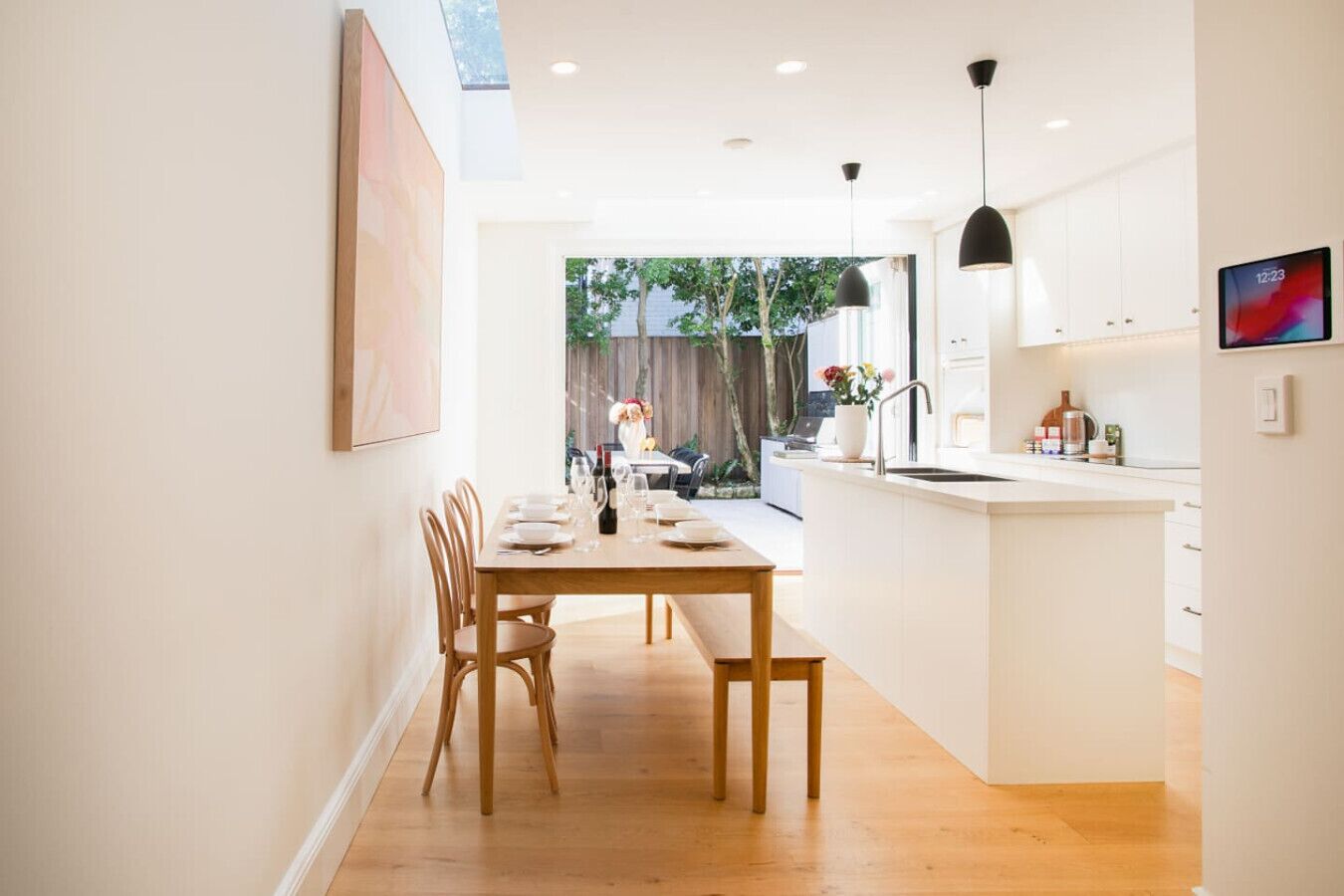 A modern kitchen with a dining area, wooden furniture, and a view into the backyard.