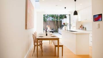 A modern kitchen with a dining area, wooden furniture, and a view into the backyard.