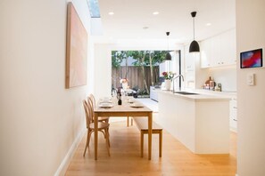 A modern kitchen with a dining area, wooden furniture, and a view into the backyard.