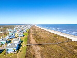 An aerial view of a coastal residential area with beachfront properties, a boardwalk, and a clear view of the ocean.