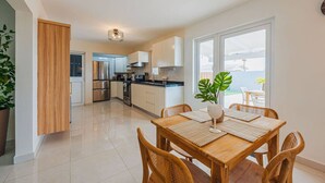 Une cuisine moderne avec des meubles blancs, des appareils en acier inoxydable et un coin repas comprenant une table et des chaises en bois.