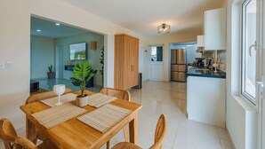 Une cuisine moderne dotée d’appareils électroménagers en acier inoxydable, un coin repas avec une table et des chaises en bois, et une grande fenêtre laissant entrer la lumière naturelle.