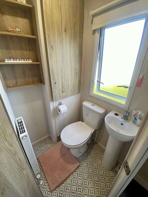 A compact bathroom with a toilet, sink, and a window providing a view. - The Bolt Hole Polperro (Polperro)