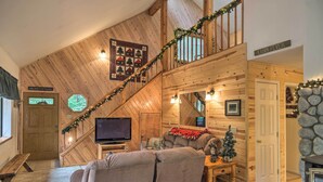 A cozy cabin interior with a wooden staircase, a television, a fireplace, and a Christmas tree. - Game Room & Deck: Pet-Friendly Camp Connell Cabin (Camp Connell)