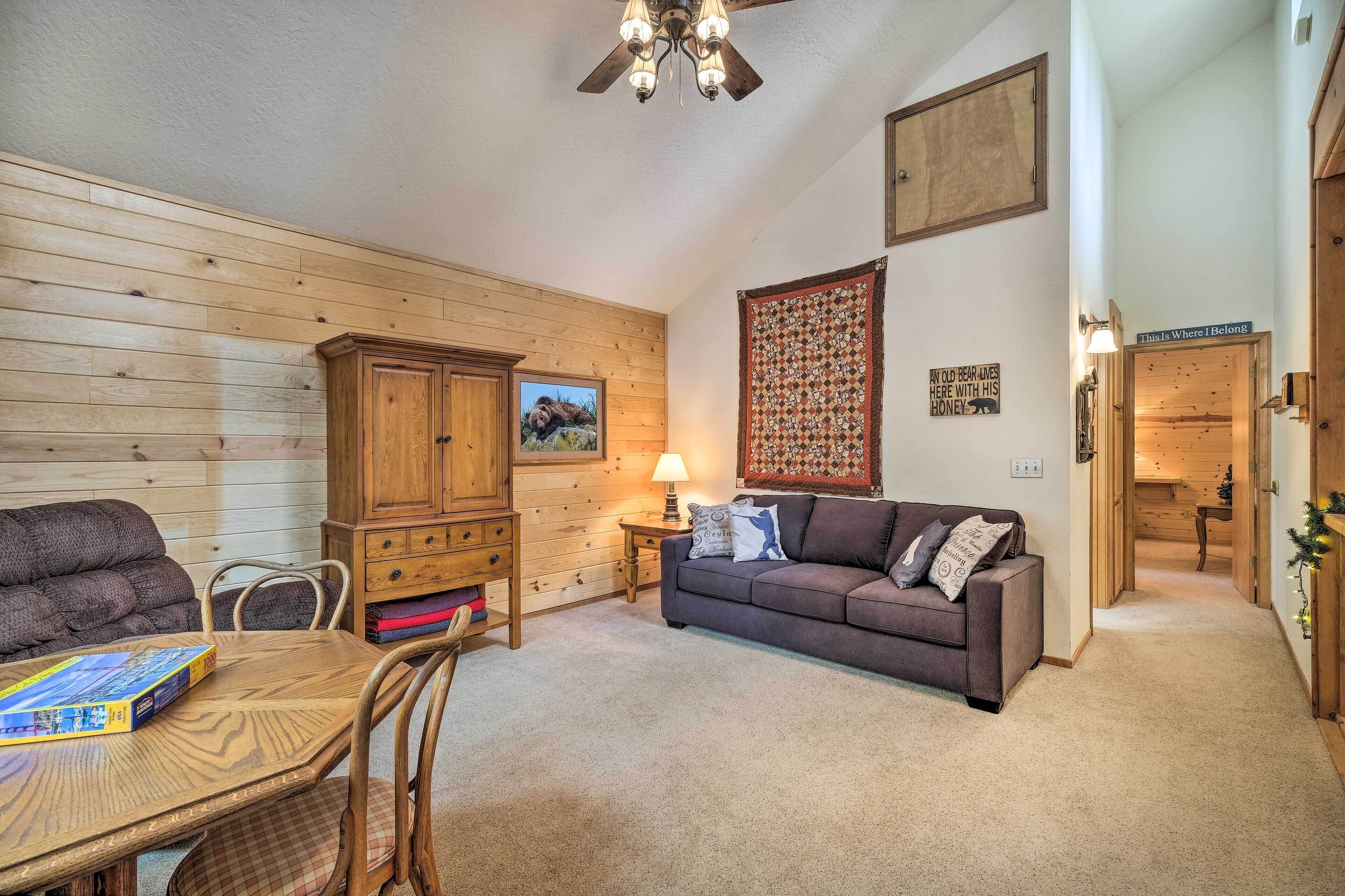 A cozy living room with a wooden wall, a sofa, a dining table, and a ceiling fan.