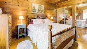 A wooden-paneled bedroom with a large bed, a nightstand, a dresser, and a mirror. - The Hideaway in Downeast Maine: Walk to Ocean (Jonesport)