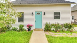 Une maison de plain-pied avec une porte d’entrée de couleur turquoise, deux fenêtres avec volets et un petit porche.