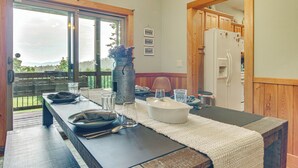 Un coin repas avec une longue table dressée pour quatre personnes, un réfrigérateur, des placards en bois et une vue à travers une porte vitrée.
