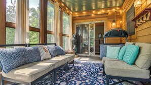 Une pièce chaleureuse avec un canapé, un banc et un divan. De grandes fenêtres et une porte donnant sur l’extérieur s’y trouvent.