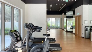 Un gimnasio con máquinas de cardio, un dispensador de agua y vistas al exterior con áreas verdes.