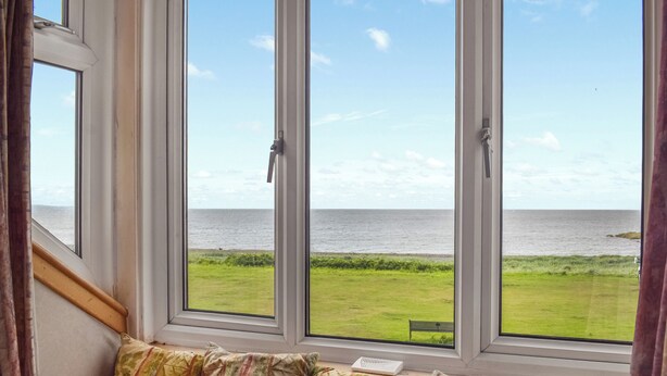 A room with a large window overlooking a grassy area and the sea.