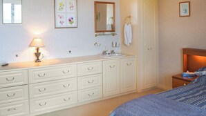 A bedroom with a bed, a bedside table, a nightstand, a dresser, a mirror, and a wall-mounted lamp.
