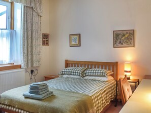 Un dormitorio con cama, mesita de noche, lámpara, silla y ventana con cortinas.
