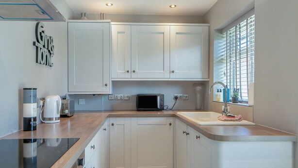 Een moderne keuken met witte kastjes, een magnetron, een waterkoker en een spoelbak.