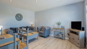 Een moderne woonkamer met een bank, stoelen, een eettafel, een televisie en een klok aan de muur.