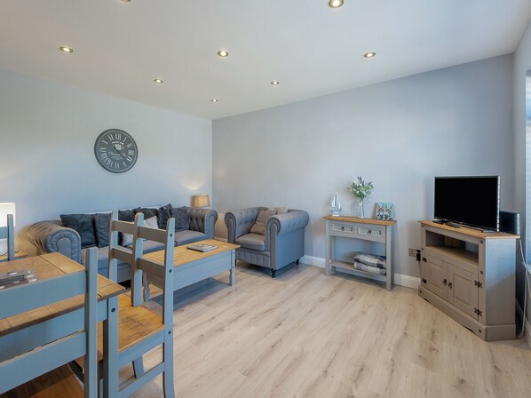 A modern living room with a sofa, chairs, a dining table, a TV, and a clock on the wall. - 2 bedroom accommodation in Snettisham (Snettisham)