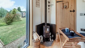 A cozy room with a wood-burning stove, a wooden door, and a view of a grassy area outside.