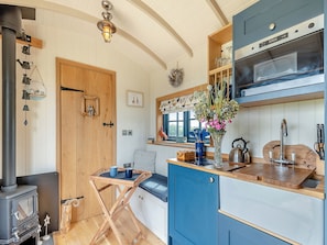 Una cocina con un estufa de leña, un armario azul y una mesa de madera con una taza azul.