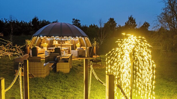 A tent with a dining area and outdoor seating, surrounded by a wooden deck and decorative lights.