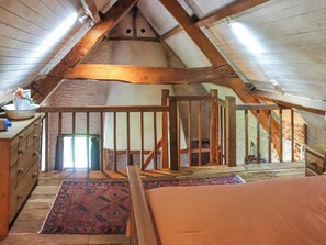 A loft bedroom with a sloped ceiling, wooden beams, a staircase, and a view of the outside. - Thatched Cottage - UK50261 (Llandeilo)