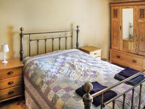 Un dormitorio con estructura de cama metálica, mesita de noche de madera, cómoda y espejo.