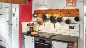 A kitchen with a black countertop, white cabinets, a red wall, and hanging pots.