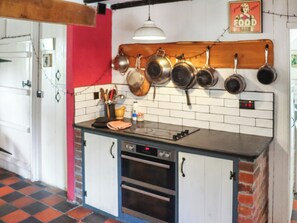 Una cocina con encimera negra, armarios blancos y una pared roja, con ollas colgando.