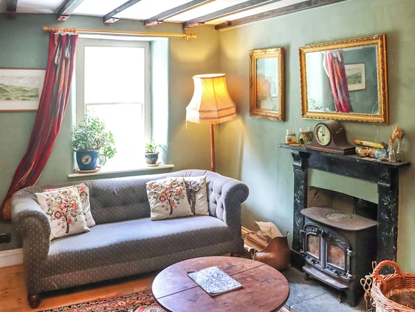 A cozy living room with a sofa, a round coffee table, a fireplace, and a window with curtains.