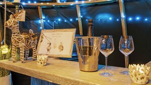 A bar area with a champagne bottle, two wine glasses, a framed welcome sign, and decorative items on a wooden counter. - Herbie's Shepherd Hut - UK50229 (Nottingham)