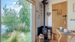 A cozy room with a large window, a wood-burning stove, and a wooden table with mugs. - Herbie's Shepherd Hut - UK50229 (Nottingham)