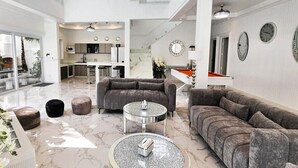 Een ruime woonkamer met een modern design, met een grote grijze modulaire bank, een ronde salontafel en een pooltafel.