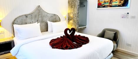 A hotel room with a large bed, a headboard, a bedside table, a chair, a wardrobe, and a painting on the wall.
