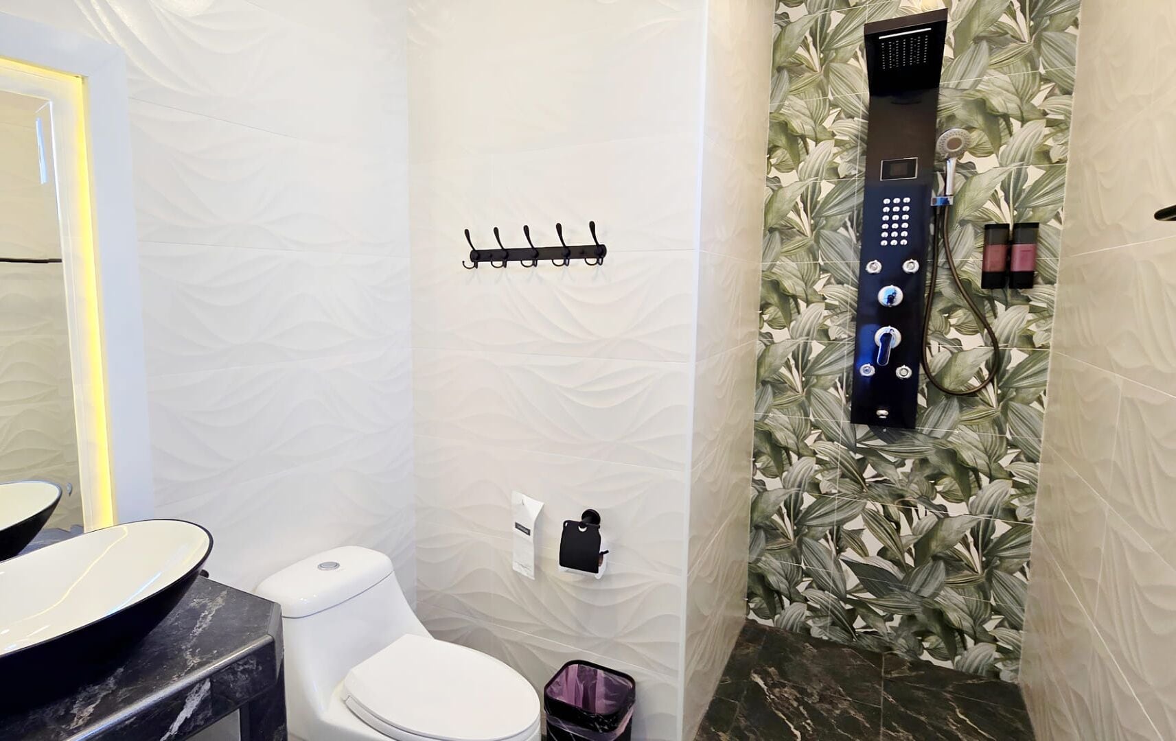 A bathroom with a toilet, a sink, a towel rack, and a shower with a control panel.