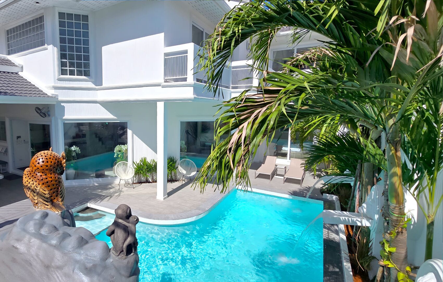 Una casa moderna con piscina, mobiliario exterior y plantas tropicales.