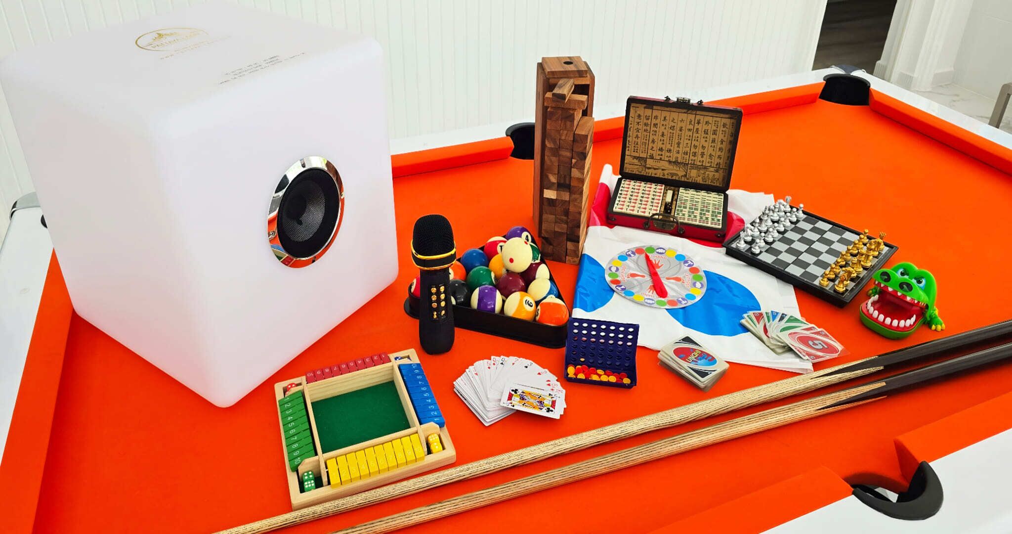 A pool table with various games and objects, including a speaker, dice, playing cards, and a toy crocodile.