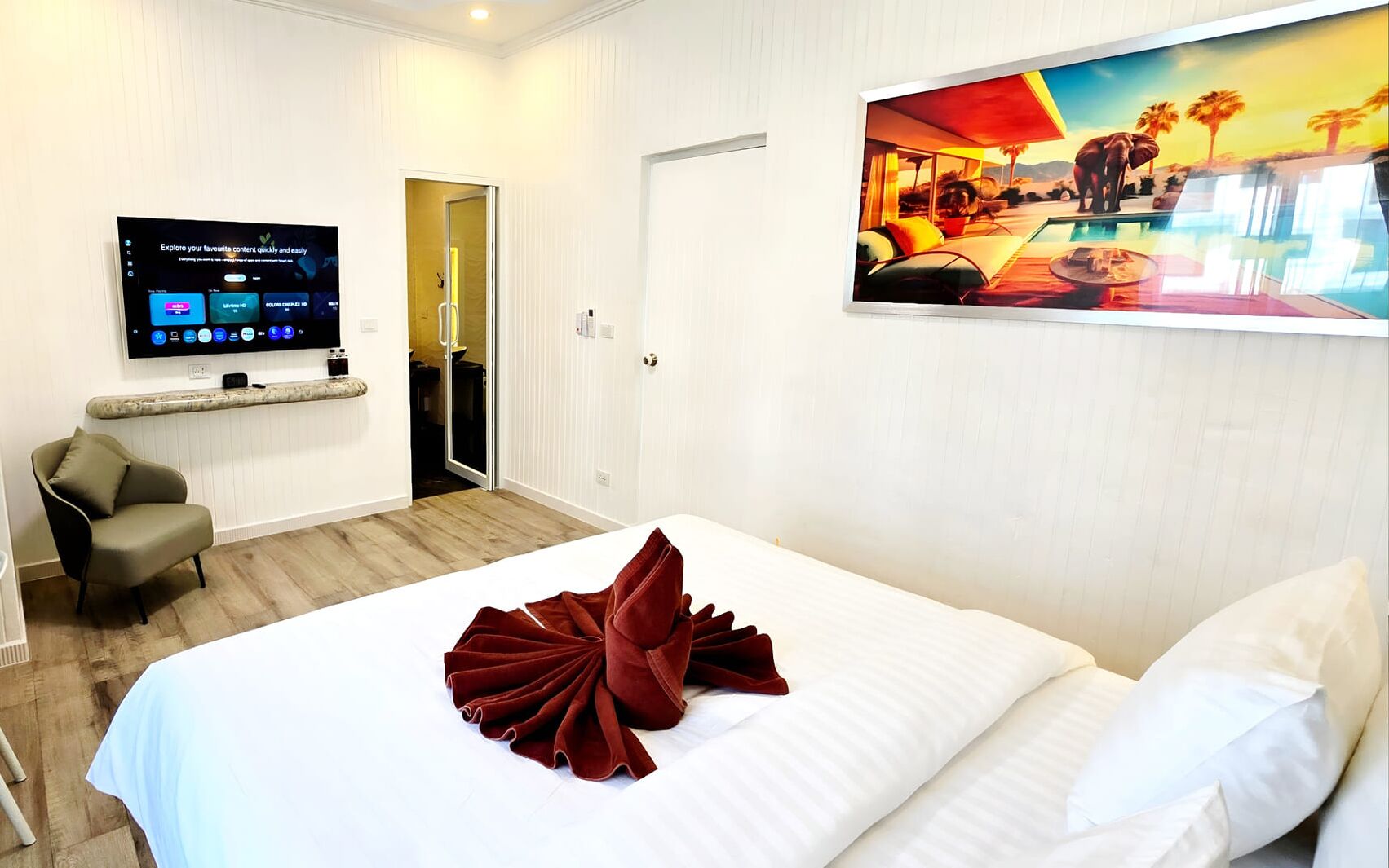 A hotel room with a bed, a TV mounted on the wall, a painting, and a chair.